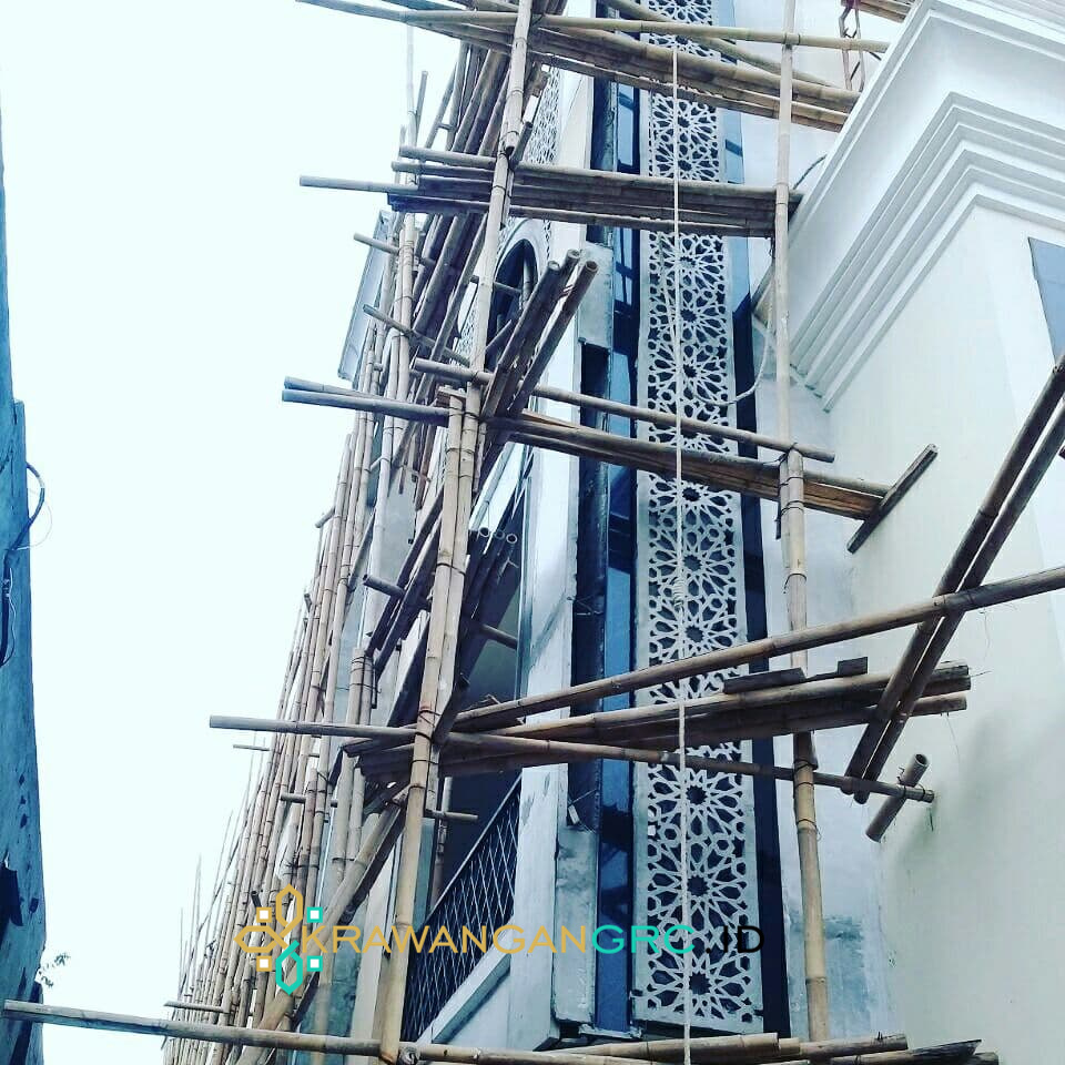 Panel krawangan GRC vertikal motif geometris pada fasad bangunan, dipasang dari perancah bambu