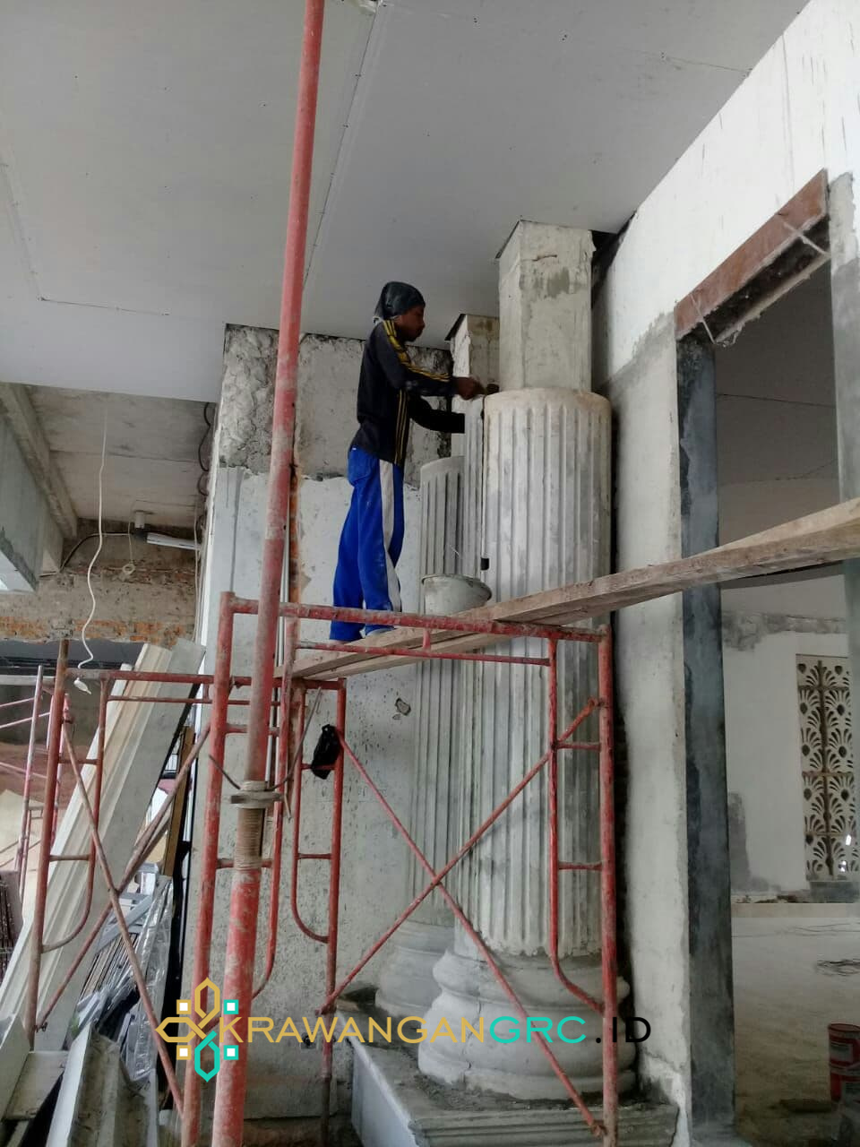 Tukang memasang pilar GRC beralur di atas perancah